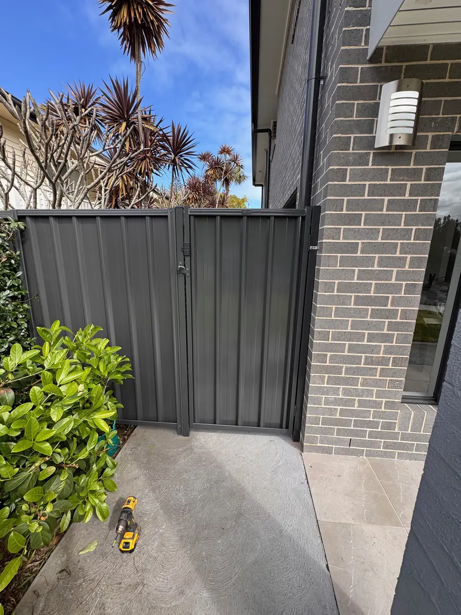 Dark metal side gate beside a brick house with a cordless drill on the concrete path