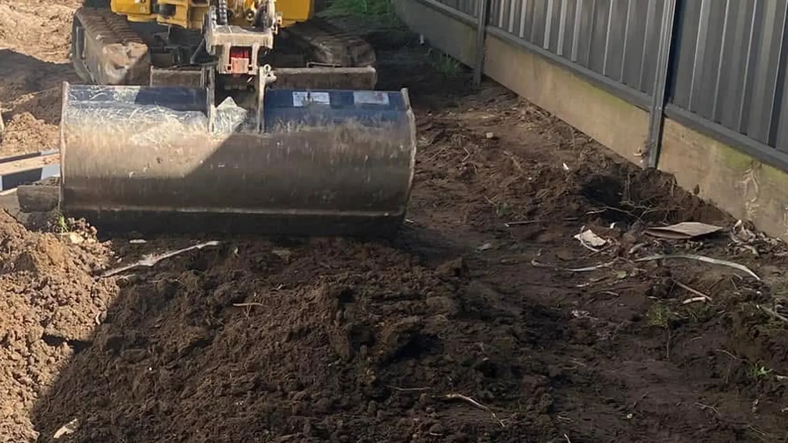 Excavator bucket and tracks on disturbed soil in a narrow side access