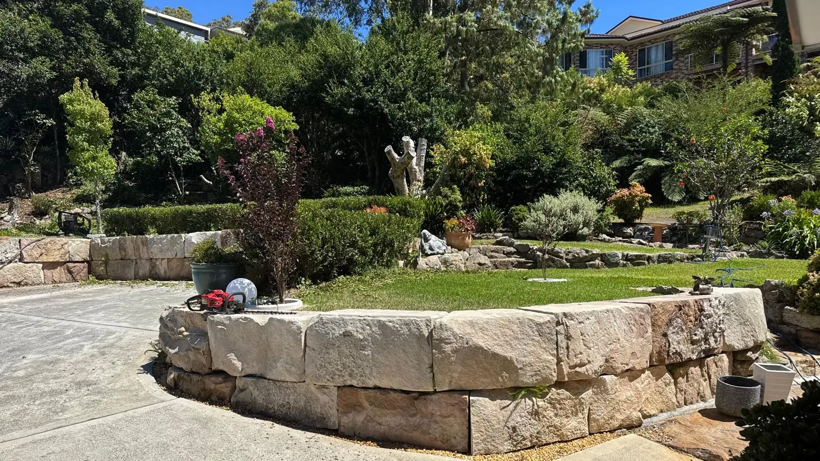 Curved sandstone retaining wall supporting a lawn and densely planted residential garden